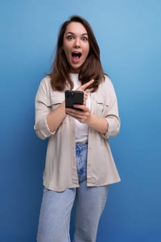 surprised caucasian young brunette woman in a shirt and jeans with a smartphone in her hands.