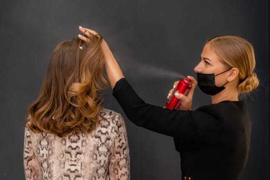 Women salon hairstyle. Hairdresser uses hairspray on client's hair in salon, Portrait of two beautiful women.