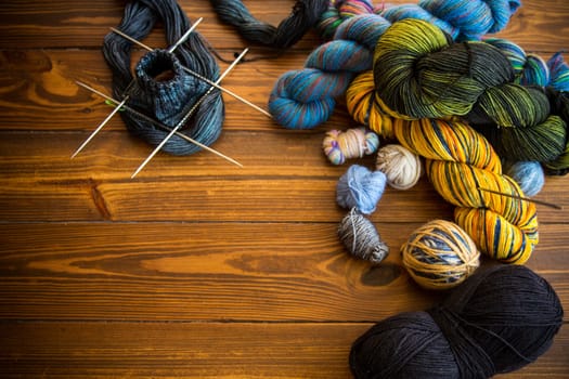 Colored threads, knitting needles and other items for hand knitting, on a dark wooden table .