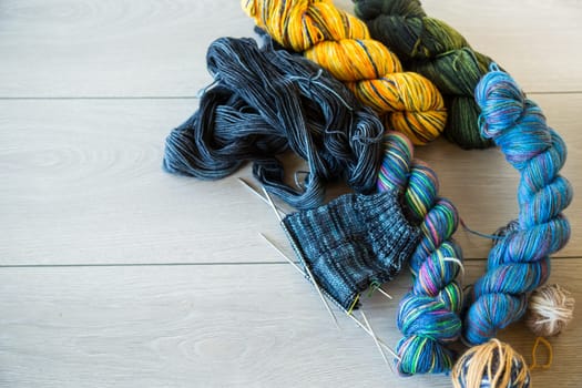 Colored threads, knitting needles and other items for hand knitting, on a light wooden table .