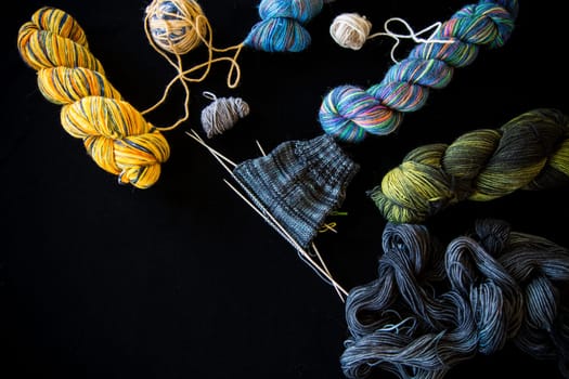 Colored threads, knitting needles and other items for hand knitting, on a black background .