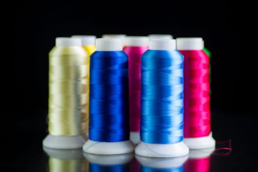 set of different color sewing threads, isolated on black background.