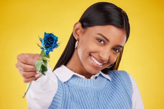 Portrait, love and rose with a woman on a yellow background in studio for valentines day. Face, blue flower and smile with a happy young female holding a plant for romance or anniversary celebration.