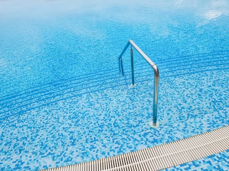 Beautiful pool with a Metal Handrails Descent and blue water at sunset. Swimming and summer rest concept