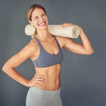 Your body is a reflection of your lifestyle. a woman holding her yoga mat against a grey background