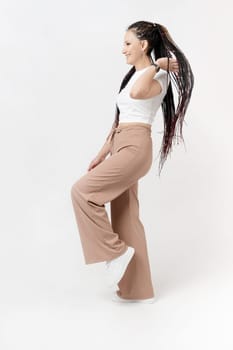 Fashionable young beautiful woman. Slim girl with dreadlocks in an active pose in a white pants and top. Fashion, clothing and style.