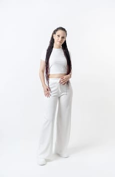 Fashionable young beautiful woman . Slim girl with dreadlocks in an active pose in a white pants and top . Fashion, clothing and style.