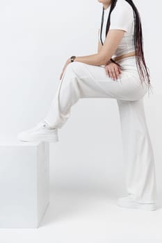 Fashionable young beautiful woman . Slim girl with dreadlocks in an active pose in a white pants and top . Fashion, clothing and style.