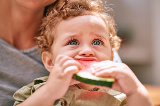 Baby, water melon and cute with an infant boy child eating fruit with his mother in the home together. Food, health and summer with a young kid biting a piece of watermelon with his mom in a house.