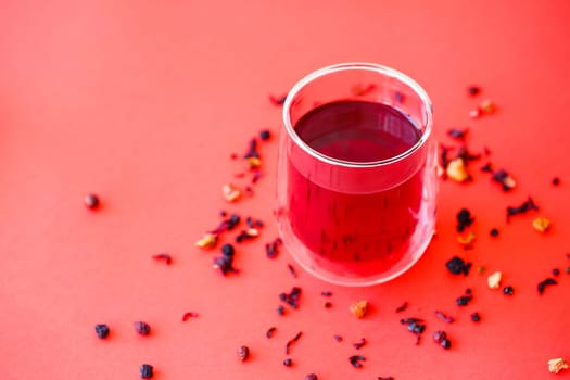 Hot hibiscus tea in a transparent glass with a double bottom on a red background