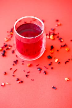 Hot hibiscus tea in a transparent glass with a double bottom on a red background
