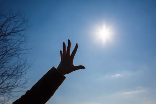 silhouetted a female hand against a blue sky and bright sun
