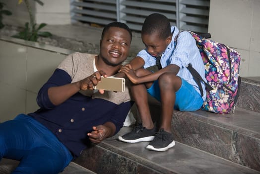 dad and urban son sitting on stairs playing game on smart phone outside, urban happy family concept,