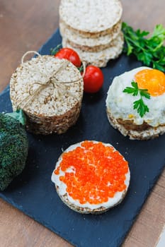 Diet rice breads, cherry tomatoes and fresh caviar and parsley on a dark background. Snack bread. View from above. Dietary fiber. Healthy Eating