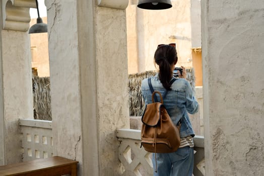 A young woman traveler with a backpack on her back walks and photographs the old narrow streets of Dubai Deira and Creek. Travel and sightseeing concept