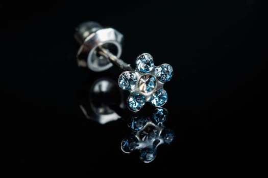 Jewelry with stone earrings, luxury silver earrings with diamonds, sapphires on a black background. Selective focus.