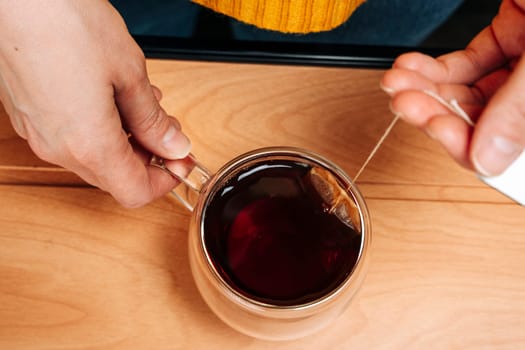 women's caring hands brew delicious fragrant tea in a glass transparent mug. tea bag for brewing. view from above. Warm soft tones. A sincere tea party in a warm atmosphere. Herbal teas