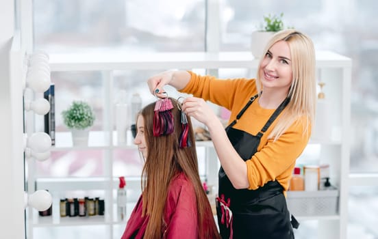 Hairdresser shows colorful samples for hair dyeing to beautiful model girl client and smiling