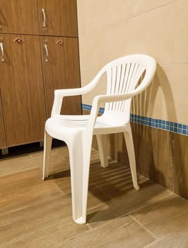 One white plastic chair stands near the wooden cabinets in the locker room of the sports club, vertical.