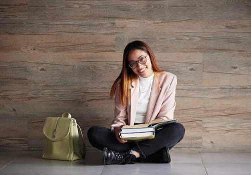 University, portrait of happy woman on floor with books on mockup space and education at college. Information, knowledge and backpack, student sitting on wall background with smile and book to study