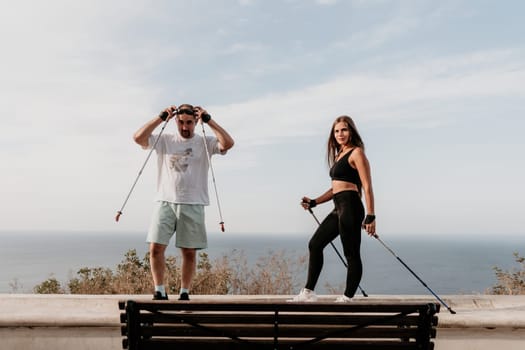 Happy Middle aged couple or friends practicing nordic walking in park near sea. Mature couple with trekking poles walking, practicing Nordic walking outdoors. Aging youthfully and sport concept.