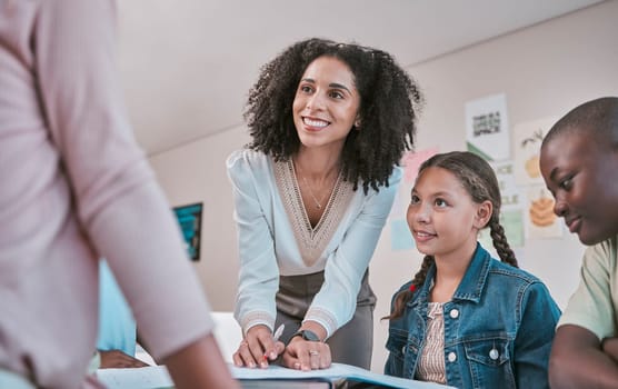 Happy teacher in classroom with children, helping students with homework and writing in book. Education in school, female educator reading kids notebook and group learning together for assessment.