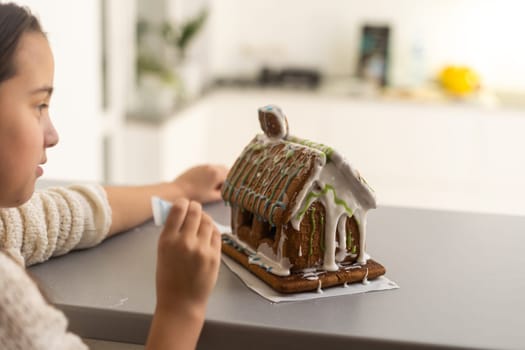 Kids baking Christmas gingerbread house. Children celebrating winter holiday at home. Decorated living room with fireplace and tree. Family activity. Little girl making cookies.