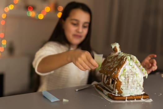 Kids baking Christmas gingerbread house. Children celebrating winter holiday at home. Decorated living room with fireplace and tree. Family activity. Little girl making cookies.