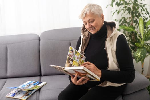 An elderly woman with nostalgia looks at old photos in a photo album or photobook - The concept of family and life values and loneliness in old age