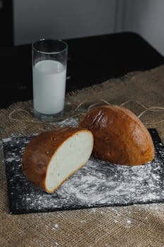 Fresh homemade crusty dark bread with seeds on a dark stand with a glass of milk on a dark background