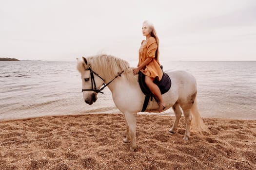 A white horse and a woman in a dress stand on a beach, with the sky and sea creating a picturesque backdrop for the scene