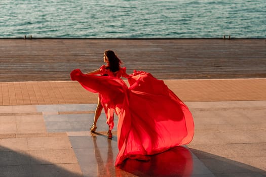 Sunrise red dress. A woman in a long red dress against the backdrop of sunrise, bright golden light of the sun's rays. The concept of femininity, harmony