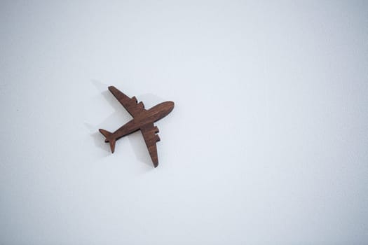 A wooden airplane figurine is glued to a wall on a white background, a place for advertising text inscription