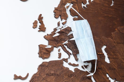 Protective antiviral mask is dressed on a wooden map of the world
