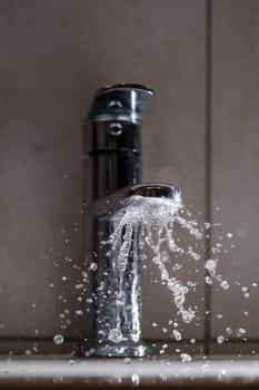 Broken water faucet in the bathroom sink. Water splashes from the silver faucet. Selective focus
