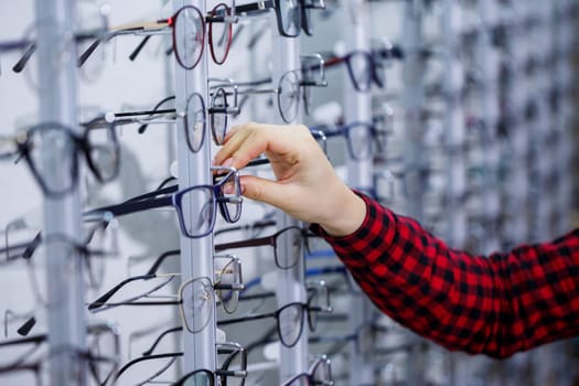 Row of glasses at an opticians. Eyeglasses shop. Stand with glasses in the store of optics. Woman's hand shows glasses. Presenting spectacles. Closeup