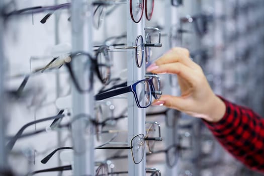 Row of glasses at an opticians. Eyeglasses shop. Stand with glasses in the store of optics. Woman's hand shows glasses. Presenting spectacles. Closeup