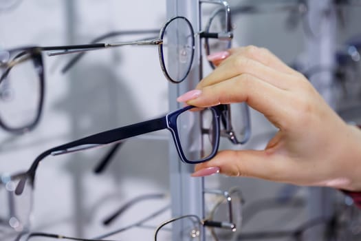 Row of glasses at an opticians. Eyeglasses shop. Stand with glasses in the store of optics. Woman's hand shows glasses. Presenting spectacles. Closeup