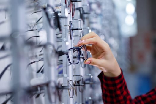 Row of glasses at an opticians. Eyeglasses shop. Stand with glasses in the store of optics. Woman's hand shows glasses. Presenting spectacles. Closeup