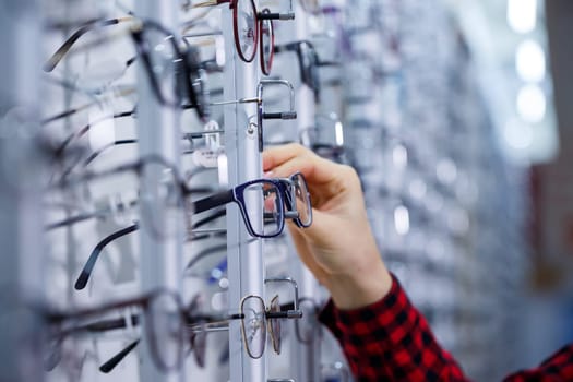Row of glasses at an opticians. Eyeglasses shop. Stand with glasses in the store of optics. Woman's hand shows glasses. Presenting spectacles. Closeup