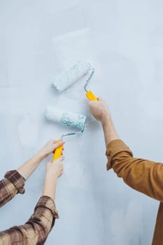 Couple in love, newlyweds in shirts and jeans in an empty room, painting white walls and renovating the interior. A man and a woman moved to a new house. Selective focus