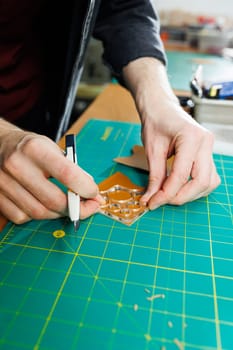 A man's hand holds pieces of leather for a leather wallet in his workshop. The process of working with natural brown leather. The craftsman holds the craft
