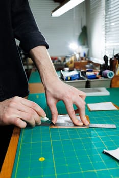 A man's hand holds pieces of leather for a leather wallet in his workshop. The process of working with natural brown leather. The craftsman holds the craft