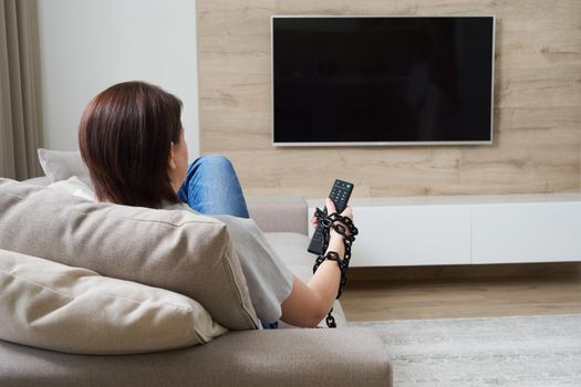 TV addiction and dependency concept. Female hand tied to the remote with the chain