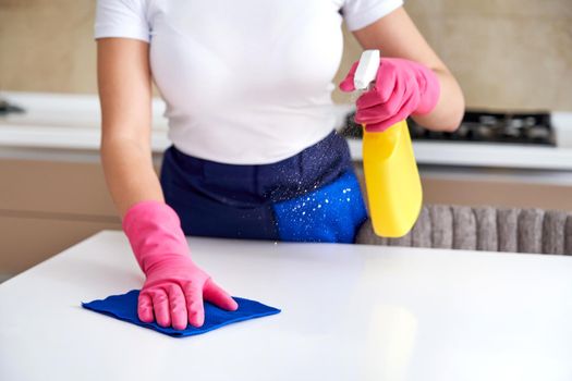 Woman wearing rubber gloves cleaning table with cloth. Disinfecting a kitchen table with bleach
