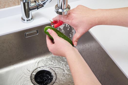 Cropped view of female hands peeling cucumber over Food waste disposer machine 