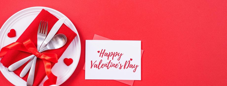 Valentine's Day holiday dating meal, banquet greeting card design concept - White plate with cutlery on red background, top view, flat lay.