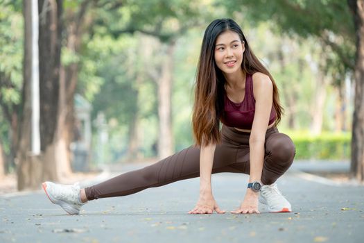 Beautiful Asian sport woman stretching right legs on road of park or garden also smile from relaxation after exercise in the morning.