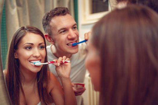 Portrait of a beautiful young happy couple brushing teeth in front of their bathroom mirror. Selective focus.
