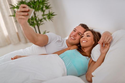 Beautiful young loving couple take a selfie in bed in the morning. 